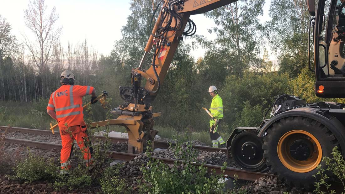 Arbete på järnväg med en traktor och träd runtomkring.